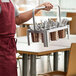 A man holding a Choice stainless steel flatware carrier with copper perforated cylinders full of utensils.
