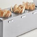 A stainless steel flatware carrier with black plastic cylinders holding wooden spoons and forks.