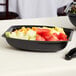 A black Cambro Camwear rectangular ribbed bowl filled with fruit on a white surface.