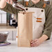 A person using a metal scoop to pour coffee beans into a brown paper bag.