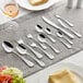 An Acopa Vittoria stainless steel oval bowl dinner/dessert spoon on a table set with silverware and a glass of wine.