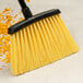 A Carlisle commercial broom with yellow and black bristles and a black handle.