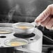 A person using the Choice 5-Cup Egg Poacher Set to put eggs into a pan.