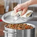 A person's hand using a white towel to remove a Choice domed aluminum pot cover from a pot of stew.