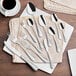 A close-up of Acopa stainless steel teaspoons on a table with silverware and a coffee cup.