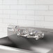A stainless steel wall mount faucet with an 8-inch swing spout and dual handles, installed above a commercial sink.