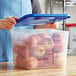 A woman holding a Vigor translucent square plastic container with apples in it with a blue lid.