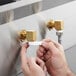 A person using a Regency wall mount faucet with a swivel gooseneck spout to fill a white plastic cup.