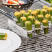 Stainless steel Outset jalapeno roaster with yellow cheese-filled green bell peppers on a grill.