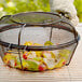 An Outset grill basket with food inside on a table.