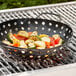 An Outset non-stick grill basket with vegetables cooking in it on a grill.