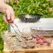 A person grilling vegetables in an Outset chrome grill basket.
