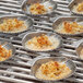 Several Outset stainless steel clam grill shells with food on a grill.