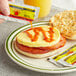 A hand pouring The Original Louisiana Brand Hot Sauce from a packet onto a breakfast sandwich.