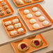 A Baker's Mark orange non-stick wire rim aluminum sheet pan holding various pastries on a table.