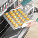 A person holding a Baker's Mark glazed aluminized steel mini muffin pan full of muffins.