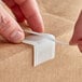 A person's hands using a white plastic edge protector on cardboard.