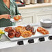 A woman holding a Baker's Mark white wire rim aluminum sheet tray of pastries on a table.
