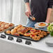 A person using a Baker's Mark black rimmed sheet pan to serve pastries on a buffet table.