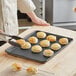 A person using tongs to take biscuits off a Baker's Mark non-stick sheet pan.
