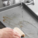 A hand using a sponge to wash a Baker's Mark non-stick bun pan on a counter.