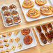 A table with trays of pastries and desserts including a muffin, cinnamon roll, and pastries.