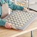 A person holding a Baker's Mark aluminized steel mini muffin pan filled with muffins.