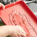 A person washing a Baker's Mark red aluminum sheet tray with water running over it.