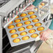 A person putting jumbo muffins in a Baker's Mark aluminized steel pan.