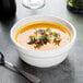 A white Tuxton china bowl of soup with a spoon.