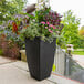 A black rectangular Mayne Kobi planter with flowers in it on an outdoor patio table.