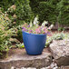 A Mayne Modesto Neptune Blue planter with pink flowers in it.