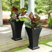 Two Mayne black square planters on a wood table with plants in them.