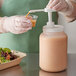 A person in gloves using a Choice condiment pump to pour liquid into a plastic container.