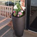 An espresso Mayne Modesto planter with flowers in it.