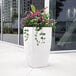 A white Mayne Kobi planter with purple flowers.