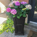 A black Mayne Fairfield planter with flowers on a table.