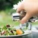 A hand holding a Libbey salt shaker over a salad.