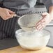 A person using a Vollrath fine mesh strainer to sift powder into a bowl.