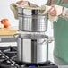 A person cooking pasta in a large silver pot.