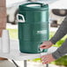 A person pouring water into a green plastic container with a white handle.