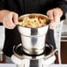 A person holding a Vollrath stainless steel food pan filled with noodles and carrots.