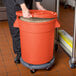 A person holding a large orange bucket with a lid.