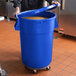 A person in a school kitchen holding a blue mobile ingredient storage bin with food inside.