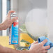 A person's hand spraying a window with a blue and white SC Johnson Windex aerosol container.