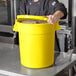 A man in a chef's uniform holding a yellow round ingredient storage bin.