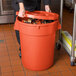 A woman in a black uniform holding an orange round ingredient storage bin with a lid.
