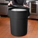 A person holding a large black container with a lid.