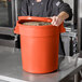 A man in a chef's uniform holding a large orange round ingredient storage bin.