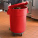 A woman in a chef's uniform holding a red mobile ingredient storage bin with the lid open.